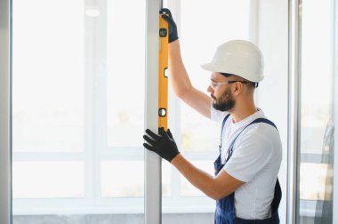 Evdeki oturma odasına plastik pencereler monte eden ya da ayarlayan işçi.