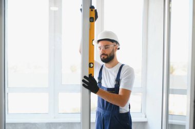 Yakışıklı genç adam yeni ev şantiyesine pencere takıyor..