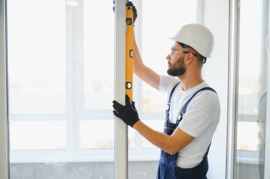 Evdeki oturma odasına plastik pencereler monte eden ya da ayarlayan işçi.