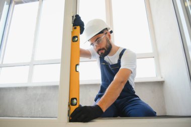 Evdeki oturma odasına plastik pencereler monte eden ya da ayarlayan işçi.