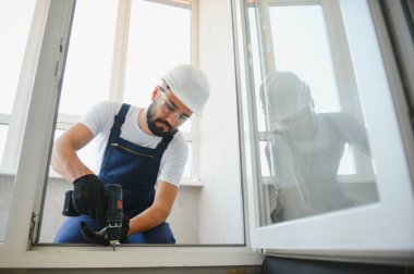Tamirci, beyaz plastik pencereyi içeri ayarlıyor. İşçi, pencereyi onarmak için tornavida kullanıyor. ev ödevi.