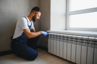 Tesisatçı radyatör tamir ediyor. Ayarlanabilir bir anahtarla musluğu sıkıyor..