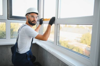 Evdeki oturma odasına plastik pencereler monte eden ya da ayarlayan işçi.