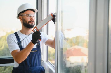 Worker sealing plastic window with caulk indoors. Installation process.