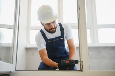 Tamirci, beyaz plastik pencereyi içeri ayarlıyor. İşçi, pencereyi onarmak için tornavida kullanıyor. ev ödevi.