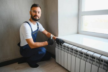 Tesisatçı radyatör tamir ediyor. Ayarlanabilir bir anahtarla musluğu sıkıyor..