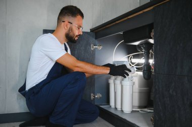 Tesisatçı su filtresi kurar ya da değiştirir. Yerleştirme su filtresi. Tamirci mutfağa su filtresi koyuyor. Ters osmoz su arıtma sisteminin kurulumu.