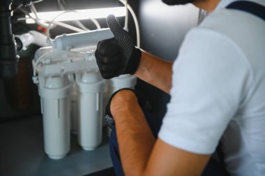 Tesisatçı su filtresi kurar ya da değiştirir. Yerleştirme su filtresi. Tamirci mutfağa su filtresi koyuyor. Ters osmoz su arıtma sisteminin kurulumu.