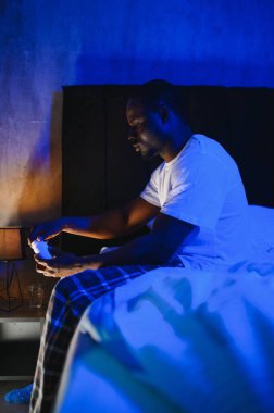 Kötü Uyku. Siyah adamın portresi, gece uyandığında evdeki yatak odasında oturuyor. Yorgun adamın baş ağrısı ve uykusuzluk sorunu var, uyuyamıyorum. Uykusuzluk Konsepti.