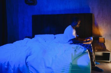 Kötü Uyku. Siyah adamın portresi, gece uyandığında evdeki yatak odasında oturuyor. Yorgun adamın baş ağrısı ve uykusuzluk sorunu var, uyuyamıyorum. Uykusuzluk Konsepti.