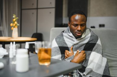 Grip ya da soğuk algınlığı olan Afrikalı Amerikalı bir adam. İlaç alır ve çay içer..
