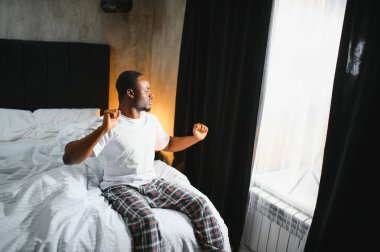 İyi sabahlar. Mutlu siyah adam uyanıyor ve kollarını gülümsüyor, büyük bir uykudan sonra dinleniyor, modern yatak odasının içinde yatıyor. Yeni Günün Başı, Dinlenme ve Sağlık Konsepti.