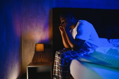 Kötü Uyku. Siyah adamın portresi, gece uyandığında evdeki yatak odasında oturuyor. Yorgun adamın baş ağrısı ve uykusuzluk sorunu var, uyuyamıyorum. Uykusuzluk Konsepti.