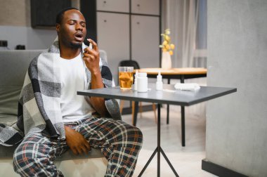 Boğaz ağrısı çeken bir adam evdeki kanepede rahatlamak için boğaz spreyi kullanıyor..