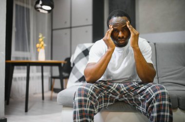 Evinde baş ağrısı çeken, şakaklarına dokunan, fotokopi çeken, geçmişi bulanık genç Afrikalı Amerikalı adama yakın çekim. Migren, baş ağrısı, stres, gerilim sorunu, akşamdan kalma konsepti