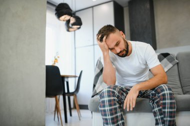 Evde baş ağrısı çeken bir adam, şakaklarına dokunuyor, fotokopi odası, bulanık arka plan. Migren, baş ağrısı, stres, gerilim sorunu, akşamdan kalma konsepti.
