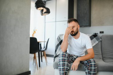 Evde baş ağrısı çeken bir adam, şakaklarına dokunuyor, fotokopi odası, bulanık arka plan. Migren, baş ağrısı, stres, gerilim sorunu, akşamdan kalma konsepti.