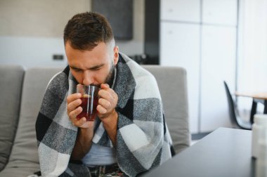 Kanepede otururken ateşi ve baş ağrısı çeken hasta bir adam. Tedavi ve hastalık kavramı.
