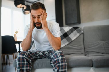 Evde baş ağrısı çeken bir adam, şakaklarına dokunuyor, fotokopi odası, bulanık arka plan. Migren, baş ağrısı, stres, gerilim sorunu, akşamdan kalma konsepti.