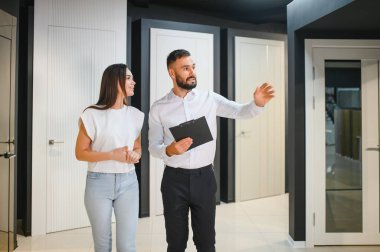 Hırdavatçıda alışveriş yapan gülümseyen genç bir kadının portresi farklı kapı seçenekleri seçiyor. Erkek danışman seçiminde yardımcı olur.