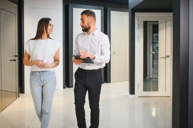 Hırdavatçıda alışveriş yapan gülümseyen genç bir kadının portresi farklı kapı seçenekleri seçiyor. Erkek danışman seçiminde yardımcı olur.