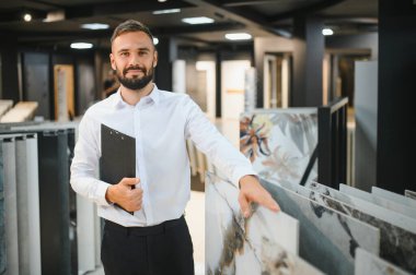 Seramik seramik satıcısının portresi. Satıcı geniş bir fayans çeşidinin arka planında duruyor..