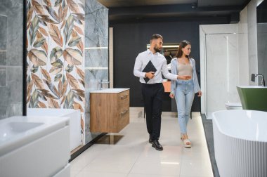 Gülümseyen kadın müşteri ve satış müdürü müşteri tuvaletini gösteriyor. Mutlu kadın alışveriş yapıyor, duş kabini seçiyor, banyo odası için mutfak gereçleri, tesisatçı yardım ediyor, danışmanlık yapıyor..