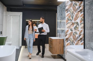 Genç çift, tesisat dükkanında bir sürü hijyenik eşya olan banyo mobilyalarını seçiyor..