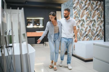 Erkek ve kadın yeni bir banyo borusu seçiyorlar. Tesisatçı dükkanında yan yana duruyorlar..