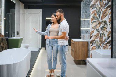 Genç çift yeni banyo mobilyalarını seçiyor. Su tesisatında beyaz akrilik banyo küvetleri var..