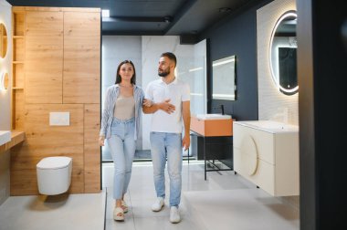 Genç çift, tesisat dükkanında bir sürü hijyenik eşya olan banyo mobilyalarını seçiyor..