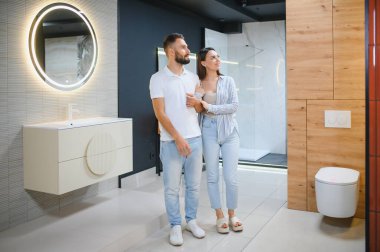 Genç çift, tesisat dükkanında bir sürü hijyenik eşya olan banyo mobilyalarını seçiyor..