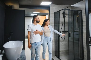 Erkek ve kadın yeni bir banyo borusu seçiyorlar. Tesisatçı dükkanında yan yana duruyorlar..