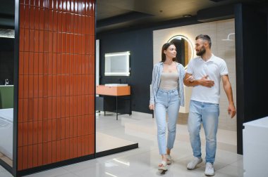 Genç çift, tesisat dükkanında bir sürü hijyenik eşya olan banyo mobilyalarını seçiyor..