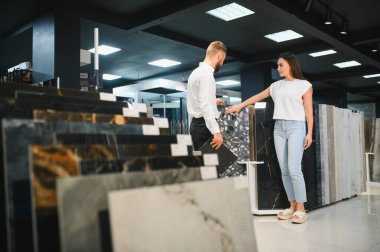 Salesman and a female customer choosing a right ceramic tile for her home, at the home design store. clipart