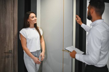 Hırdavatçıda alışveriş yapan gülümseyen genç bir kadının portresi farklı kapı seçenekleri seçiyor. Erkek danışman seçiminde yardımcı olur.