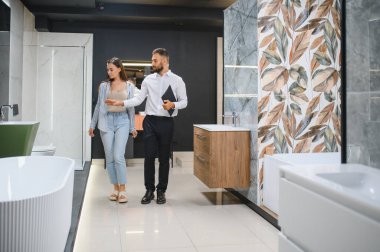 Genç çift, tesisat dükkanında bir sürü hijyenik eşya olan banyo mobilyalarını seçiyor..