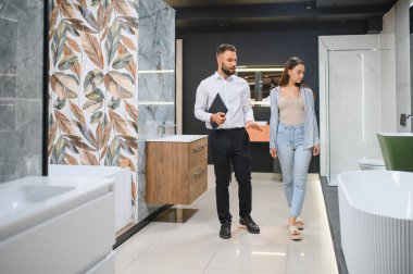 Genç çift, tesisat dükkanında bir sürü hijyenik eşya olan banyo mobilyalarını seçiyor..