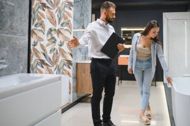 Gülümseyen kadın müşteri ve satış müdürü müşteri tuvaletini gösteriyor. Mutlu kadın alışveriş yapıyor, duş kabini seçiyor, banyo odası için mutfak gereçleri, tesisatçı yardım ediyor, danışmanlık yapıyor..