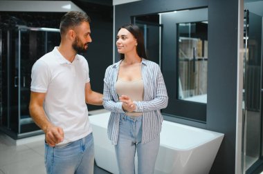 Genç çift yeni banyo mobilyalarını seçiyor. Su tesisatında beyaz akrilik banyo küvetleri var..