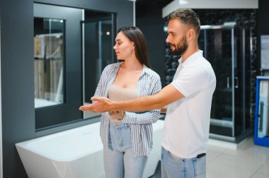 Genç çift yeni banyo mobilyalarını seçiyor. Su tesisatında beyaz akrilik banyo küvetleri var..