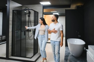 Genç çift yeni banyo mobilyalarını seçiyor. Su tesisatında beyaz akrilik banyo küvetleri var..