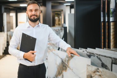 Seramik seramik satıcısının portresi. Satıcı geniş bir fayans çeşidinin arka planında duruyor..
