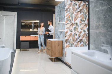 Genç çift, tesisat dükkanında bir sürü hijyenik eşya olan banyo mobilyalarını seçiyor..