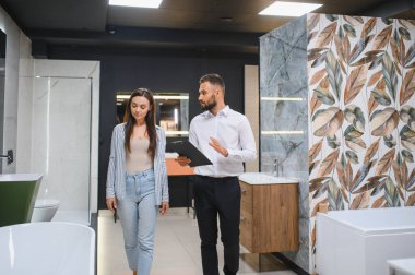 Gülümseyen kadın müşteri ve satış müdürü müşteri tuvaletini gösteriyor. Mutlu kadın alışveriş yapıyor, duş kabini seçiyor, banyo odası için mutfak gereçleri, tesisatçı yardım ediyor, danışmanlık yapıyor..