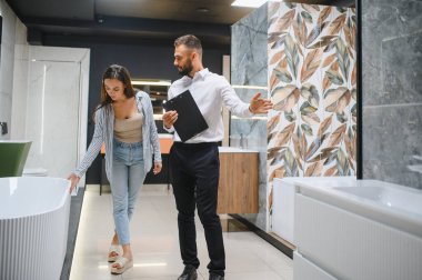 Genç çift, tesisat dükkanında bir sürü hijyenik eşya olan banyo mobilyalarını seçiyor..