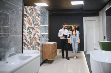 Gülümseyen kadın müşteri ve satış müdürü müşteri tuvaletini gösteriyor. Mutlu kadın alışveriş yapıyor, duş kabini seçiyor, banyo odası için mutfak gereçleri, tesisatçı yardım ediyor, danışmanlık yapıyor..