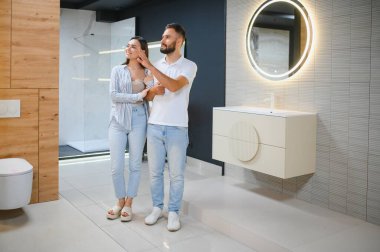 Genç çift, tesisat dükkanında bir sürü hijyenik eşya olan banyo mobilyalarını seçiyor..