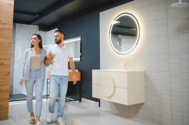 Genç çift, tesisat dükkanında bir sürü hijyenik eşya olan banyo mobilyalarını seçiyor..
