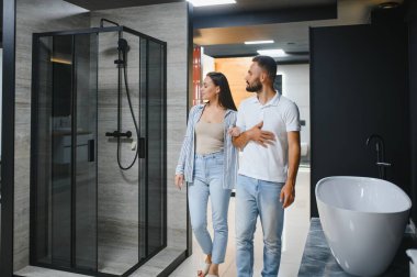 Genç çift yeni banyo mobilyalarını seçiyor. Su tesisatında beyaz akrilik banyo küvetleri var..